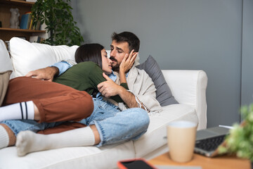 Fototapeta premium Couple goals simple living. Two young people couple man and woman, boyfriend and girlfriend lying on the sofa in cozy apartment enjoying their time together. People in love spending weekend activities