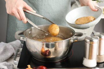 Woman putting raw potato into pot on stove, closeup