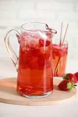 Tasty strawberry lemonade in jug, glass and berries on white wooden table