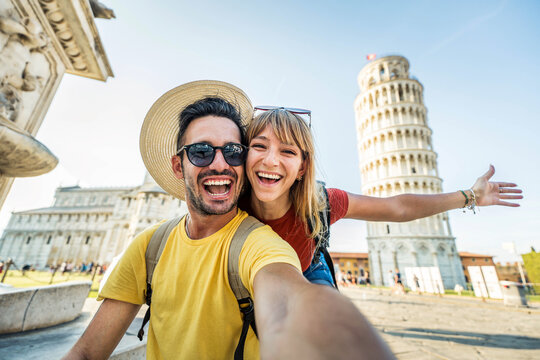 Happy tourist couple taking selfie picture in front of the famous leaning Tower and Pisa cathedral - Summertime holidays, tourism and technology concept -