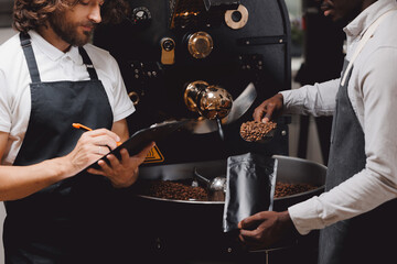 Process working in coffeestore roasting factory. Two workers in uniform packing fresh coffee beans in bag
