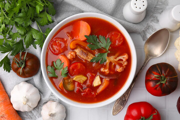 Delicious homemade stew in bowl, spoon and ingredients on white tiled table, flat lay