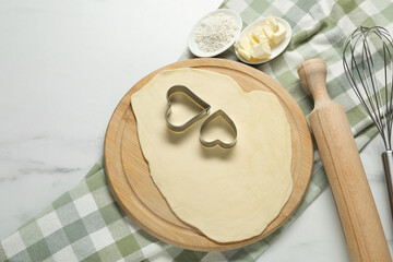 Raw dough, cookie cutters, flour, butter, whisk and rolling pin on white marble table, flat lay