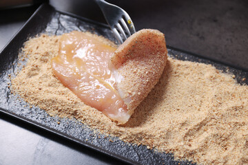 Making schnitzel. Coating slice of meat with bread crumbs at dark table, closeup