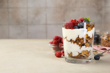 Tasty yogurt with fresh berries, granola and mint in glass on gray textured table, space for text