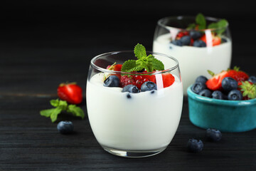Tasty yogurt with fresh berries and mint in glasses on black wooden table, closeup