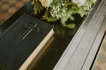 Bible with cross on black leather cover and rose bouquet on black wooden coffin