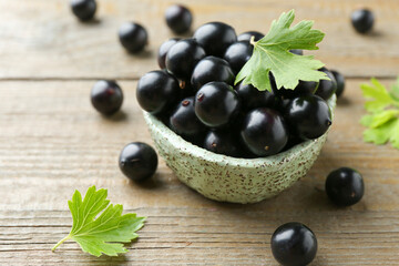 Fresh ripe black currant berries and leaves on wooden table, closeup