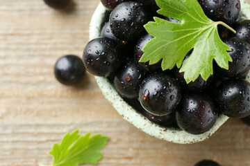 Fresh ripe black currant berries and leaves on wooden table, closeup