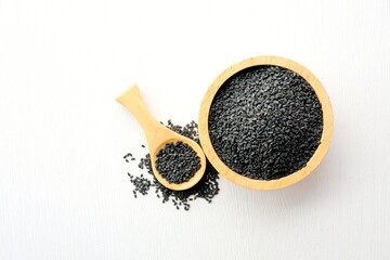 Black Sesame Seeds in a wooden bowl with a wooden spoon on white background