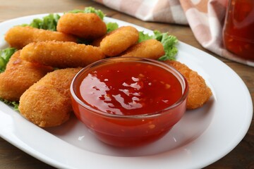 Tasty chicken nuggets with chili sauce and lettuce on table, closeup