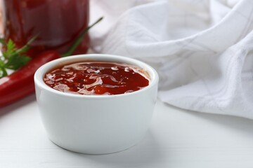 Spicy chili sauce in bowl on white wooden table, closeup