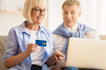 Obraz premium Modern grandparents. Mature couple shopping online on laptop, woman holding credit card