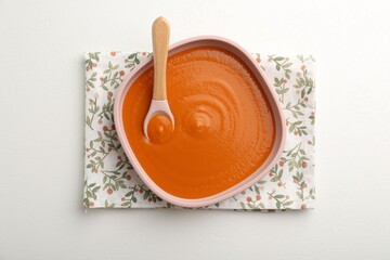 Delicious baby food in bowl on white table, top view