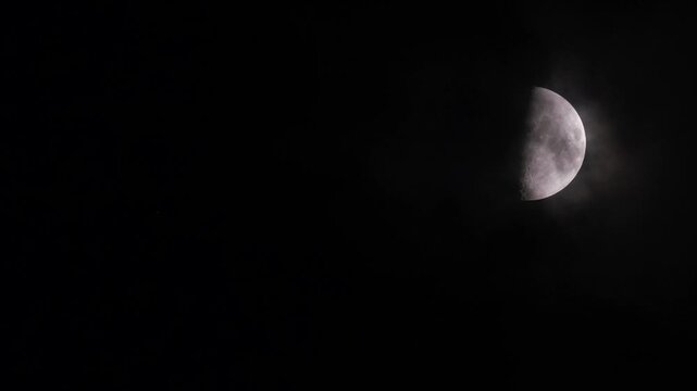 First quarter moon or waxing gibbous with amazing craters moving among mysterious clouds at night. Telephoto view, real midnight footage with black background. Creepy halloween sky, astrology concept.