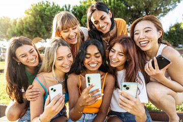Happy group of young women using smart mobile phone device outside - Laughing friends watching funny social media reel with smartphone - Youth culture life style concept with teens holding mobile cell