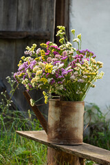 Bouquet of multicolored kermek Limonium  flowers in an old rusty garden watering can on a bench. rustic style.