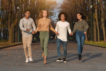 Fototapeta premium Crazy multiracial teen friends running towards camera, public park background, panorama