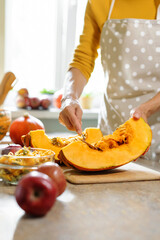 Closeup of female hands with spoon removing seeds from cutting pumpkin. Fall time, pumpkin recipe