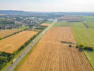 Aerial perspective showing a highway bordered by fields of hay bales, with rural landscape...