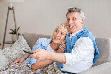 Relaxed senior couple watching television, sitting on sofa and enjoying weekend at home