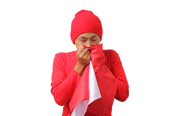 Young Indonesian man in a red long sleeve shirt and beanie is kissing the Indonesian flag, celebrating Indonesia's Independence Day on 17 August. The scene is isolated on a white background.