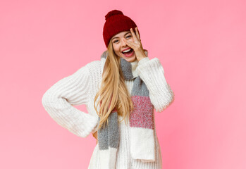 Pretty young woman in warm sweater looking through fingers, yellow studio background