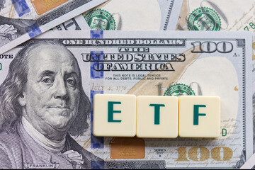 ETF, abbreviation for exchange-traded fund, word written on plastic blocks on US dollars background.