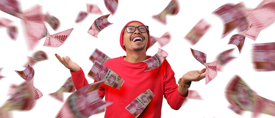Asian man stands with Indonesian Rupiah banknotes flying around him, creating a money shower effect against a white background. Concept of financial success, prosperity, and Indonesia Independence Day
