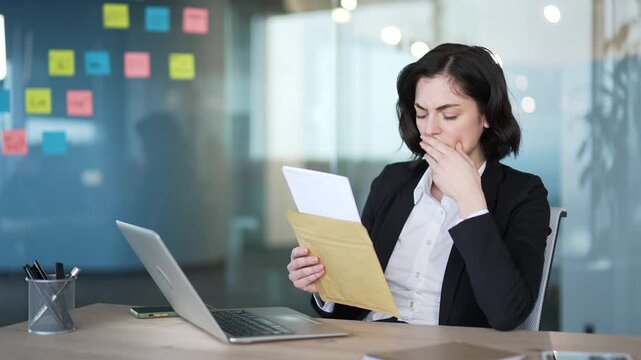Professional woman in office reading letter with bad news, showing stress and concern. Represents business stress, disappointment and corporate challenges. Emotional response to unexpected information