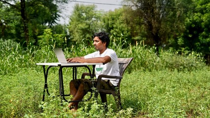 Indian young boy doing work from home. Man sitting on office table at garden doing work on internet