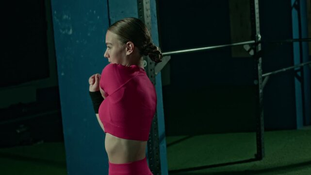 Medium shot of Caucasian sporty girl in tight pink crop top doing cross body arm stretch warmup exercise while training at gym