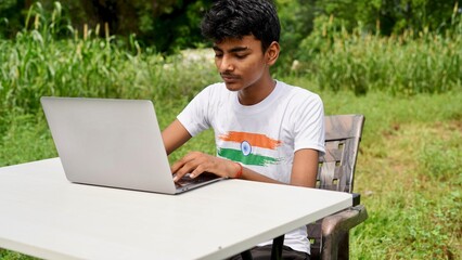 Indian young boy doing work from home. Man sitting on office table at garden doing work on internet