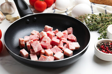 Pieces of fresh bacon in frying pan and peppercorns on white table, closeup