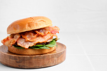 Delicious burger with bacon and greens on white table, closeup. Space for text