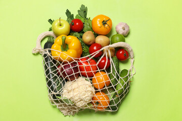 Delivery of vegetarian products. String bag with different vegetables and fruits on green background, top view