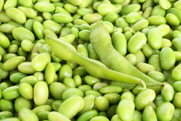 Raw green edamame pods on soybeans as background, closeup