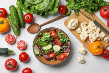 Healthy vegetarian food. Salad in bowl and vegetables on white tiled table, flat lay