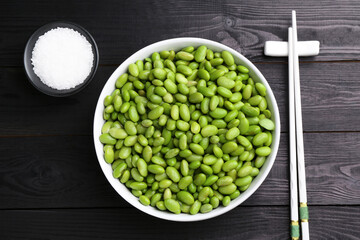 Raw green edamame soybeans, salt and chopsticks on wooden table, flat lay
