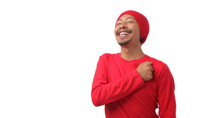 Happy Indonesian man in a red long sleeve T-shirt and beanie hat, with Indonesia flag, puts his...