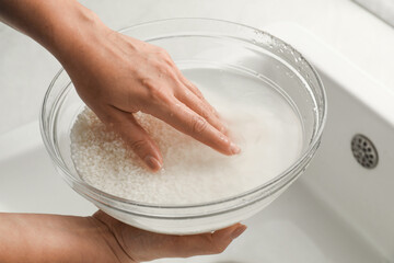 Woman rinsing rice in bowl above sink, closeup