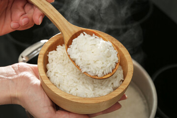 Woman taking boiled rice from pot into bowl, closeup