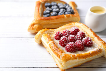 Tasty puff pastries with berries on white wooden table, closeup