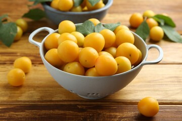 Tasty ripe plums and leaves in colander on wooden table, closeup