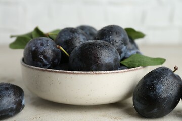 Ripe plums in bowl on light table, closeup