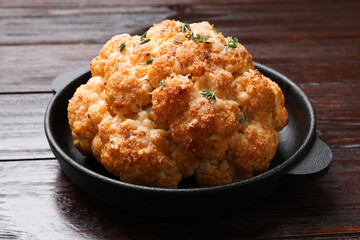 Delicious baked cauliflower in baking dish on wooden table, closeup