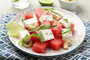 Delicious watermelon salad with feta cheese, cashew nuts and spices on light table, closeup