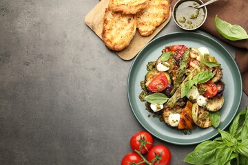 Delicious salad with grilled vegetables, pesto sauce, basil and bread on gray textured table, flat lay. Space for text