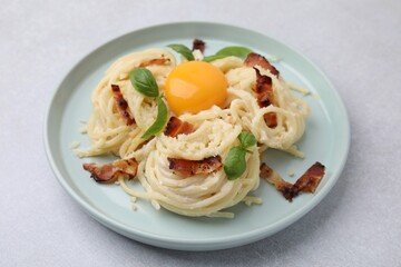 Delicious pasta Carbonara with egg yolk, bacon and basil on light gray table, closeup