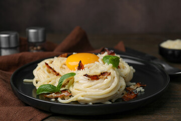 Delicious pasta Carbonara with egg yolk, bacon and basil on wooden table, closeup